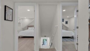 A modern, well-lit room with a bed, a small table, and a door leading to another room. - Seaside Heights' Palm Tree Paradise: 3BR (Seaside Heights)