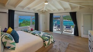 Une chambre avec un grand lit, une vue sur la mer et un balcon équipé de chaises.