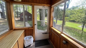Una habitación con paneles de madera, una puerta que da al exterior, un reloj en la pared y una ventana con vistas a una casa y árboles.