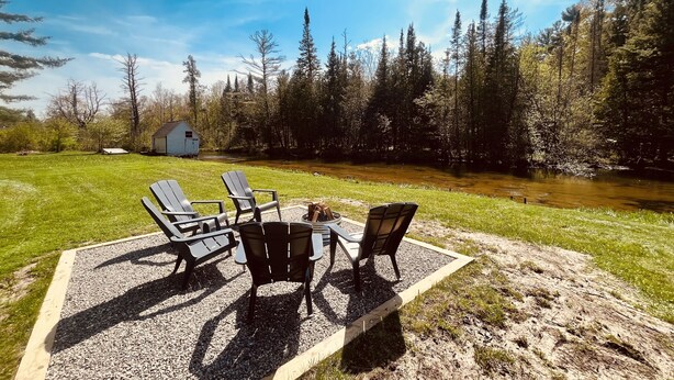 Un espacio al aire libre con sillas Adirondack y un hogar de fuego, rodeado por un patio de grava y un césped.
