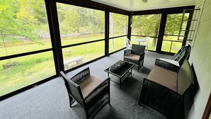 Una habitación luminosa con ventanas amplias, mobiliario de mimbre y vistas a un área con césped y árboles.