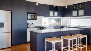 A modern kitchen with dark cabinetry, a central island with stools, and a microwave above the counter. - Salty Ocean View Escape - Torquay (Surf Coast)