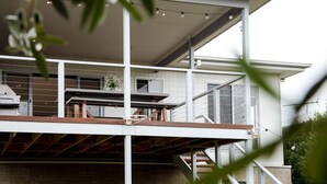 A modern multi-story building with a balcony, outdoor seating area, and string lights. - Torquay Beach Holiday Homebase (Surf Coast)