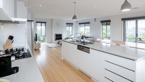 A modern kitchen with a central island, built-in appliances, and large windows offering views of the outdoors. - Torquay Beach Holiday Homebase (Surf Coast)
