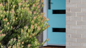 A modern building with a teal door and a brick wall. - Torquay Beach Holiday Homebase (Surf Coast)