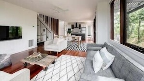 Ein modernes Wohnzimmer mit Sofa, Couchtisch und Fernseher. Eine Treppe führt zu einer oberen Ebene.