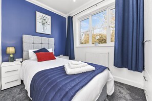 Cozy retreat with a large bed, blue accent wall, and framed artwork.