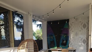 Un espace extérieur aménagé avec des meubles en osier, une table en verre et un kayak suspendu au mur.
