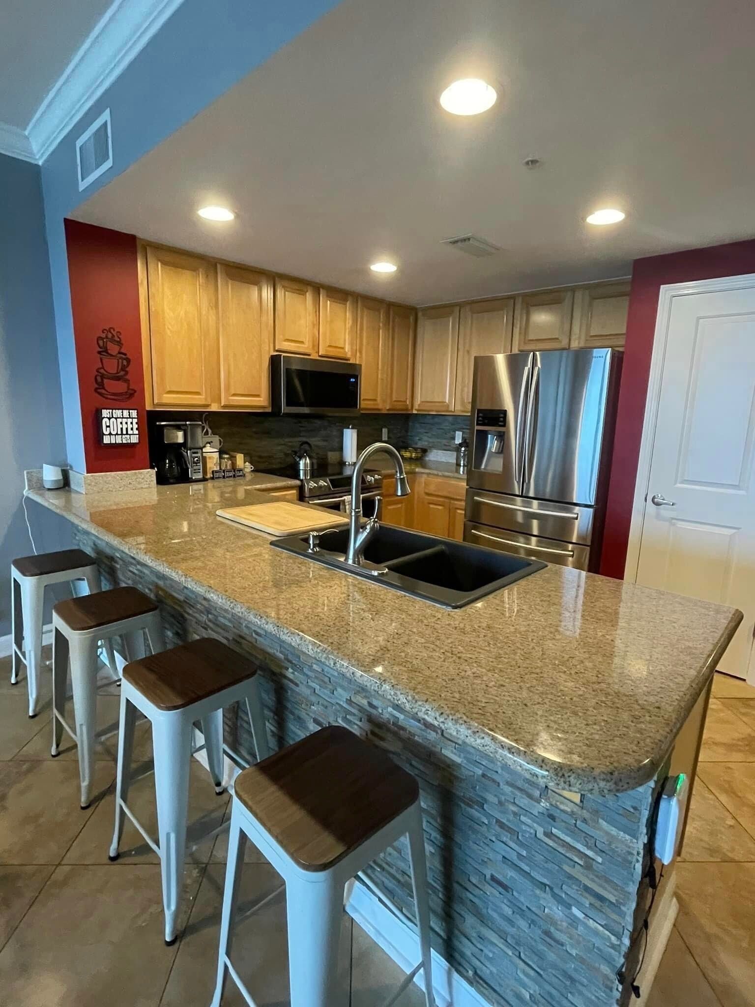 A modern kitchen with granite countertops, stainless steel appliances, and a bar area with stools.