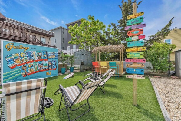 A colorful signpost with various restaurant names, a beach-themed sign, and a beach chair area. - Seaside Heights' Paradise House: 5BR (Seaside Heights)