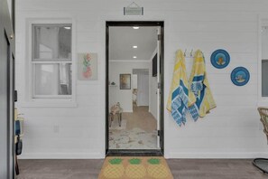 A doorway leading to a room with a pineapple-themed doormat, a sign above the door, and towels hanging on the wall. - Seaside Heights' Paradise House: 5BR (Seaside Heights)
