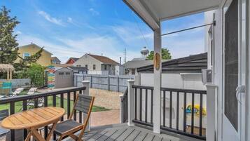 Une terrasse extérieure couverte, avec une table et des chaises, une clôture en bois et des maisons en arrière-plan.