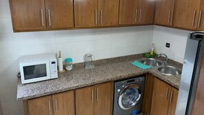 A kitchen with wooden cabinets, a microwave, a washing machine, a sink, and a faucet. - Spacious 3-bedrooms apartment (Tétouan)