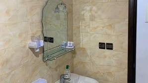 A bathroom with beige marble tiles, a white sink with a mirror above it, and a glass shelf with toiletries. - Spacious 3-bedrooms apartment (Tétouan)