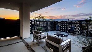 Eine Terrasse im Freien mit Blick auf den Sonnenuntergang, einem schwarzen, gemusterten Zaun und moderner Möbel.