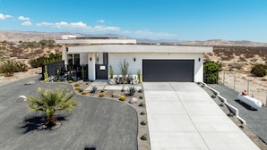 Ein modernes Haus mit Garage, Auffahrt und einem angelegten Garten mit Kakteen und einer Palme.