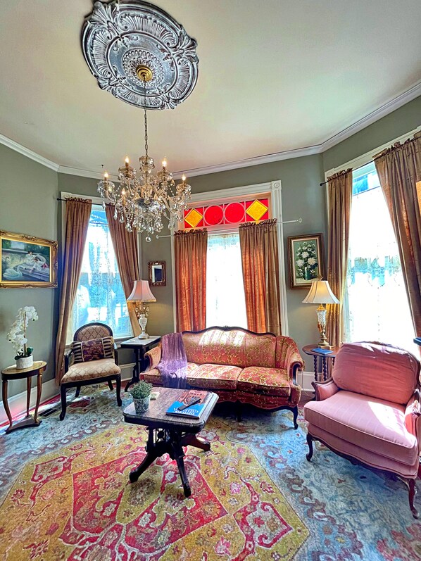 Amplia sala de estar con candelabro, alfombra estampada y muebles clásicos.