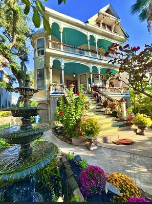Un edificio de dos plantas con un balcón y una fuente en el jardín.