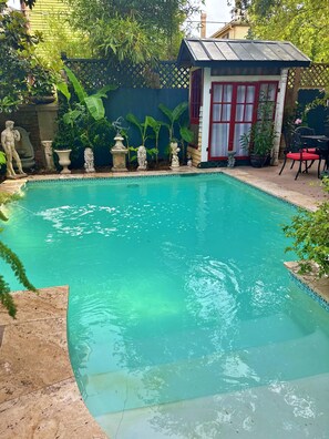 Una piscina rectangular con agua azul cristalina, rodeada de baldosas de piedra. Hay estatuas y macetas a lo largo del borde de la piscina.