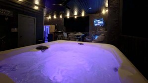 Un jacuzzi con ventilador de techo, una pantalla de televisión y una zona de estar con sillas y una mesa.