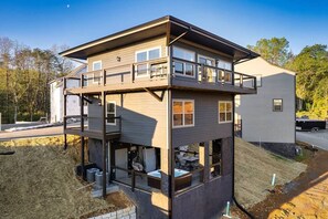 A multi-story house with a balcony on the upper level, a covered outdoor area, and a garage. - Lux Treehouse Cabin, Hot Tub, Sauna, Arcade (Sevierville)