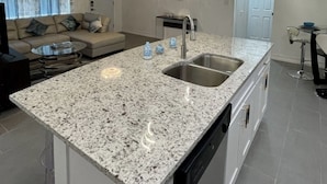 A modern kitchen with a granite countertop, stainless steel sink, and a dishwasher. - Relaxing Home Near Universal (Orlando)