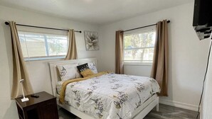 A bedroom with a bed, a nightstand, a ceiling light, and two windows with curtains. - Relaxing Home Near Universal (Orlando)