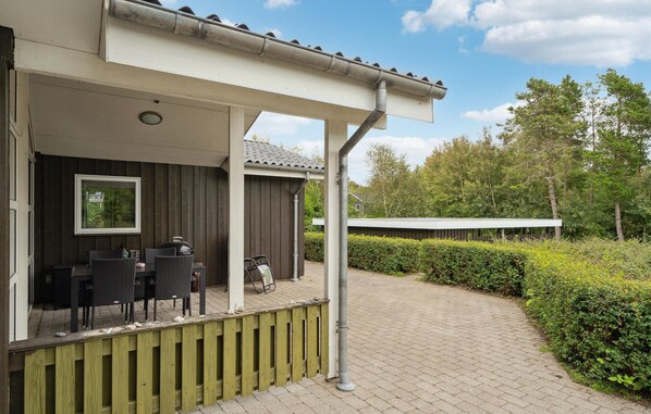 Un espace extérieur aménagé, abrité et doté d’une pergola, d’un barbecue et d’une vue sur une zone boisée.