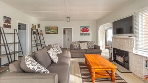 Een woonkamer met een bank, een salontafel, een open haard en een aan de muur bevestigde televisie.