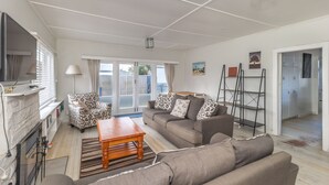 Een moderne woonkamer met een bank, fauteuil en salontafel. Er is een open haard, een televisie en een balkon met uitzicht.