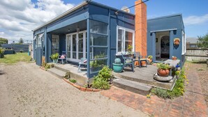 Een modern huis met een blauwe gevel, een bakstenen schoorsteen en een overdekte veranda met zitplaatsen.
