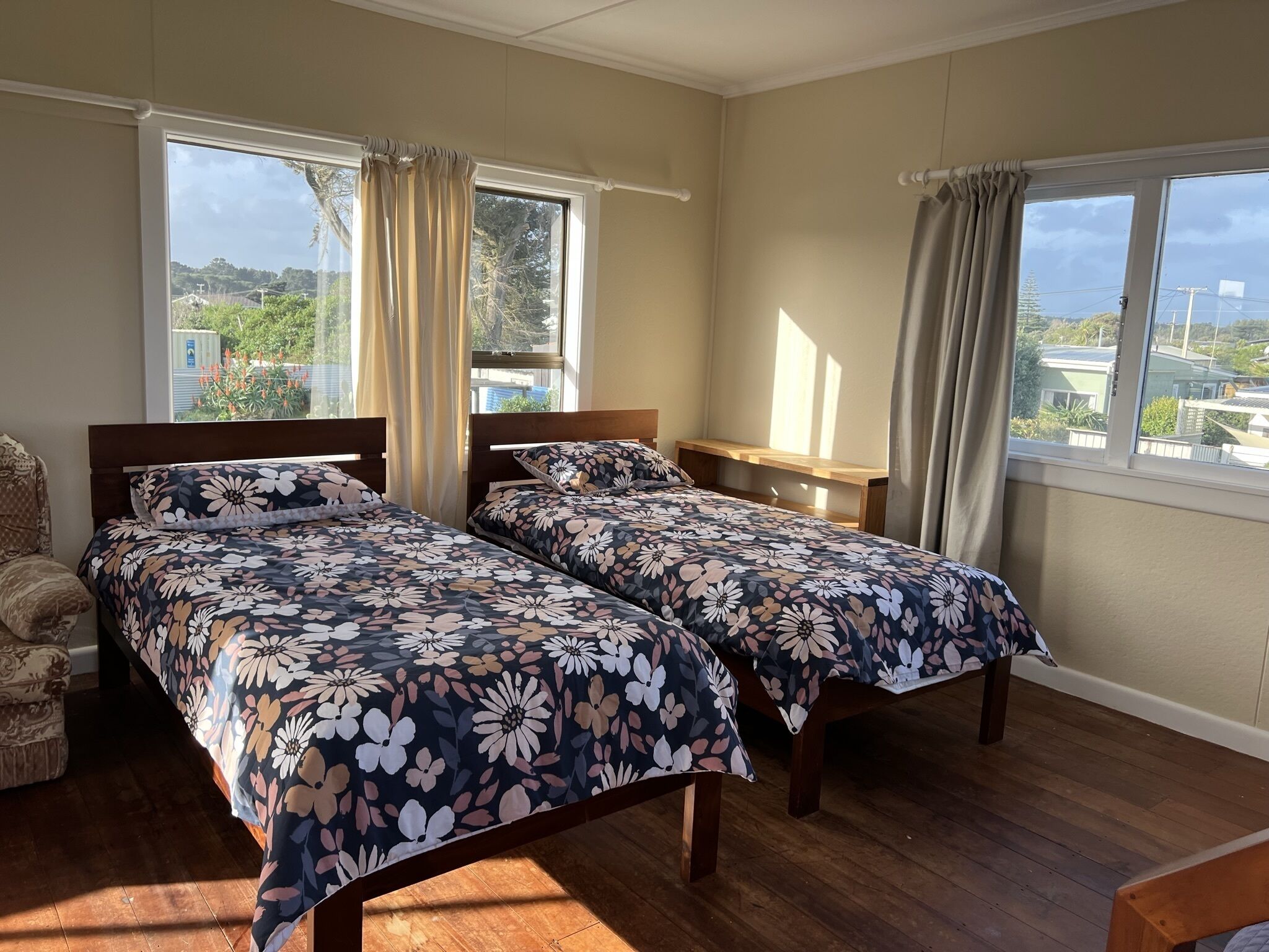 A bedroom with two beds, wooden headboards, a wooden nightstand, and a window with curtains.