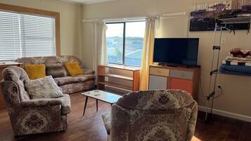 A living room with a sofa, armchair, coffee table, and a TV on a stand.