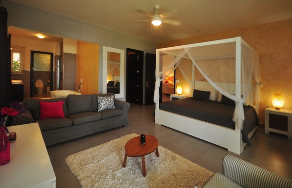 A modern living room with a grey sofa, a white daybed with a canopy, a wooden coffee table, and a white rug.