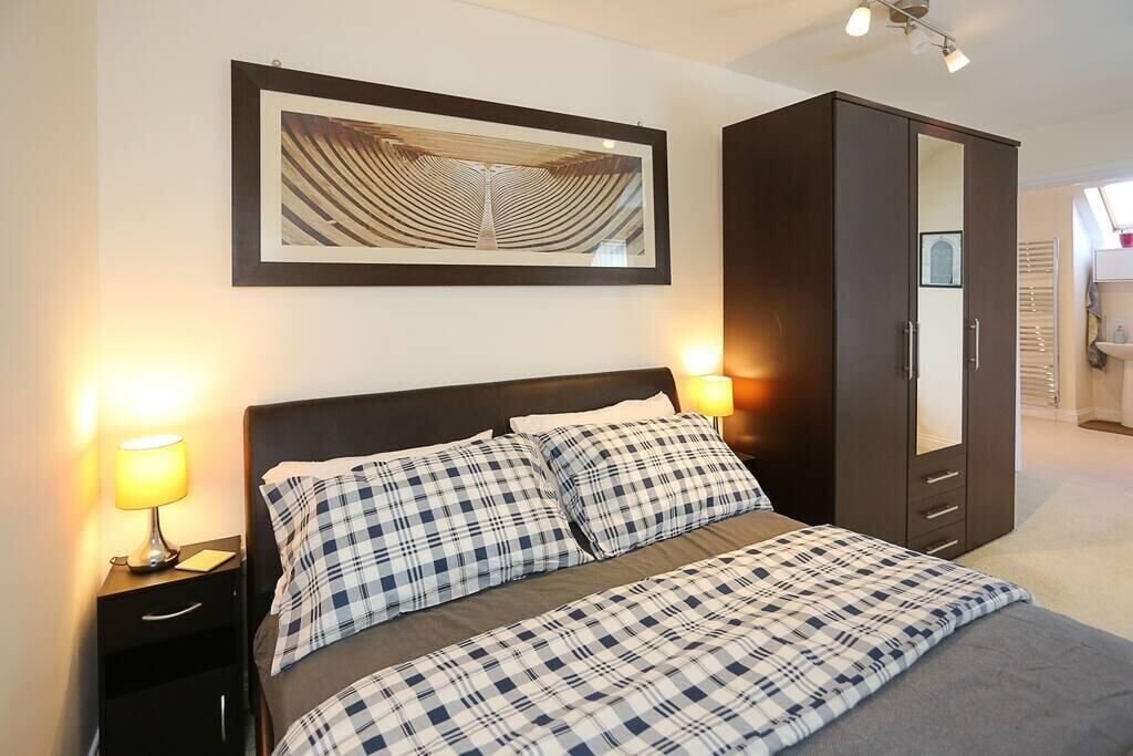 A neatly made bed with checkered bedding, a dark wardrobe, a framed artwork on the wall, and bedside lamps.