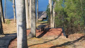 Un espace extérieur isolé, doté d’une terrasse en bois, d’une table et de chaises, et entouré d’arbres et d’une étendue d’eau.
