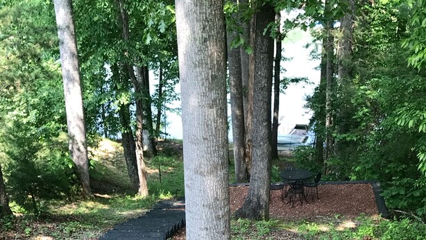 Un sentier en bois traverse une zone boisée, et une table et des chaises sont disposées à proximité.