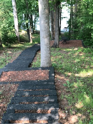 A wooden pathway in a wooded area with a table and chairs set up nearby.