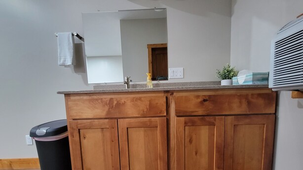 Een keuken met houten kastjes, een aanrecht, een prullenbak, een spoelbak en een spiegel.