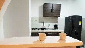 Una cucina con un piano di lavoro bianco, due tazze beige, un frigorifero nero e un pensile in legno scuro sopra il lavello.