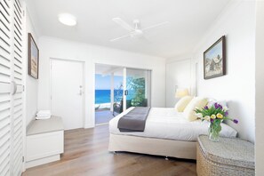 A bedroom with a bed, a bedside table, a vase of flowers, a ceiling fan, and a view of the ocean through a sliding door. - Ocean Panorama With Private Pool! (Sunshine Beach)