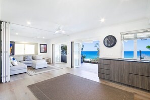 A modern living space with a sofa, a dining area with a view of the ocean, and a kitchen with a clock.