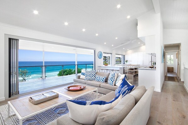 A modern living room with a large window overlooking the ocean, a kitchen area, and a dining space.