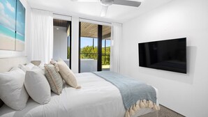 A bedroom with a bed, a ceiling fan, a TV, and a view of greenery outside.