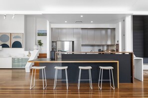 A modern kitchen with stainless steel appliances, a central island with bar stools, and a minimalist design. - Luxury & Breathtaking ocean views (Sunshine Beach)
