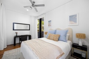 A bedroom with a bed, a ceiling fan, a bedside table, a lamp, and a window with a view. - Luxury & Breathtaking ocean views (Sunshine Beach)