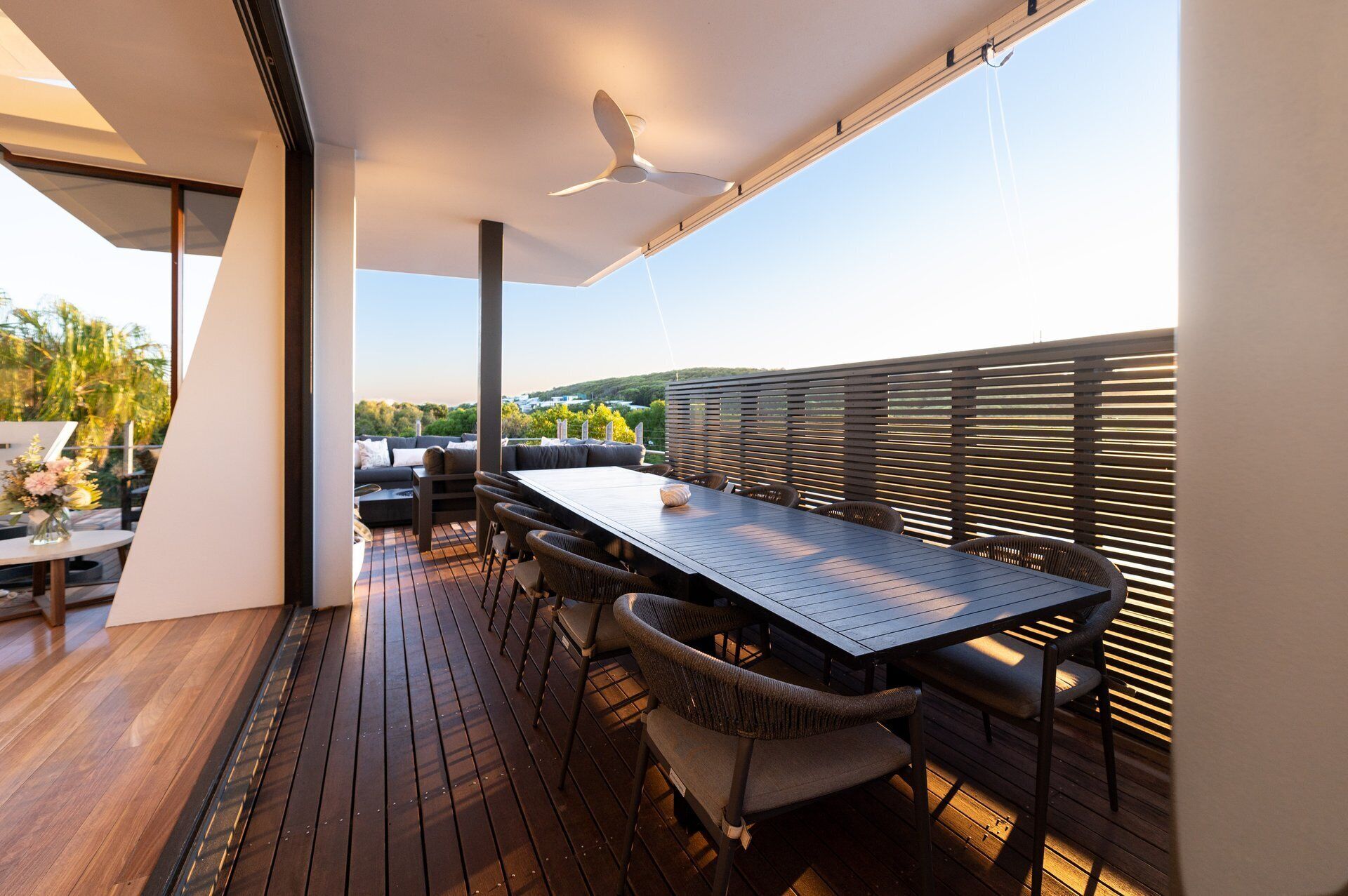 Een modern overdekt terras met een eettafel, stoelen en een plafondventilator.