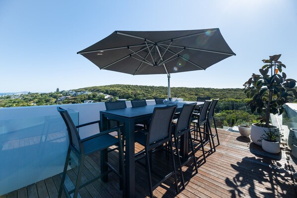 A rooftop terrace with a table and chairs, a large umbrella, and potted plants.