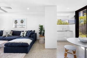 A modern living room with a dark blue sofa, a white coffee table, and a kitchen area with a sink and countertop. - Luxury & Breathtaking ocean views (Sunshine Beach)