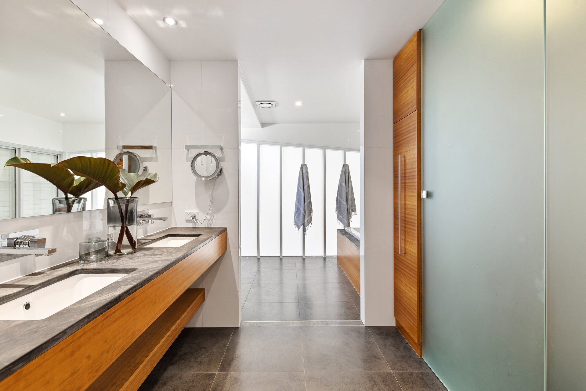 Une salle de bain moderne avec un grand miroir, deux lavabos, une douche et une vue sur l’extérieur.